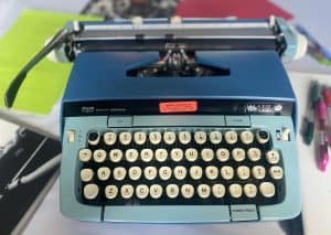 Typewriter on a desk in a vintage office setting, featuring a blue Smith-Corona Galaxy Twelve typewriter for nostalgic office decor or collectible purposes.