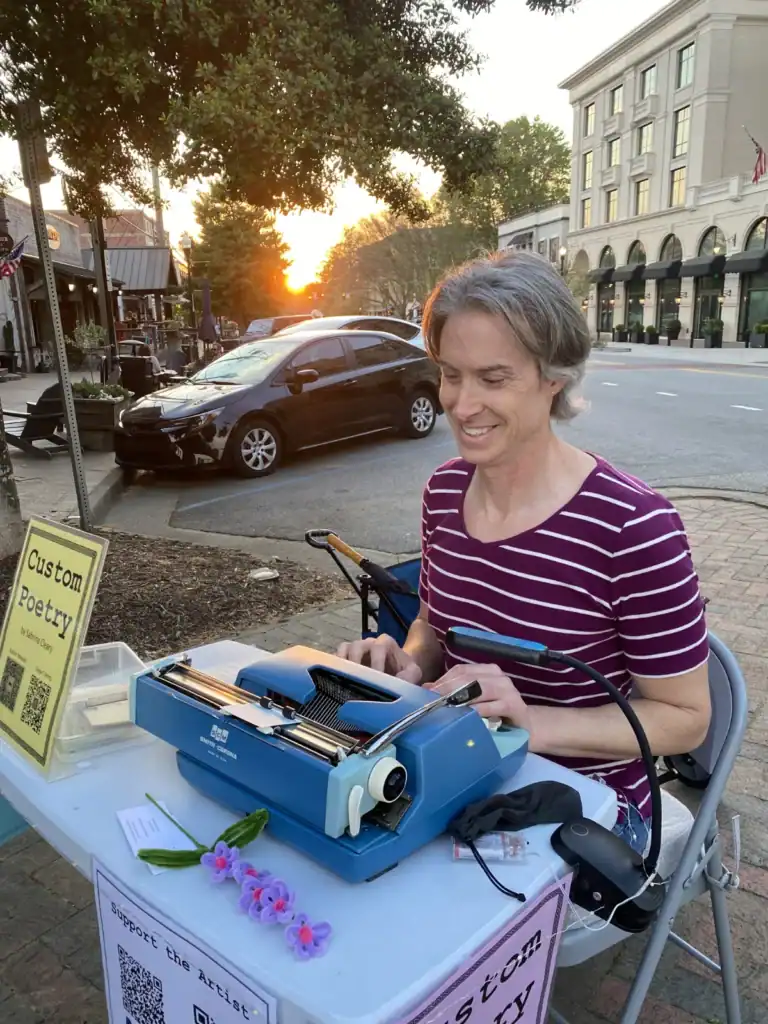 Sabrina Cleary creating custom poetry on a blue typewriter in downtown Alpharetta at sunset.