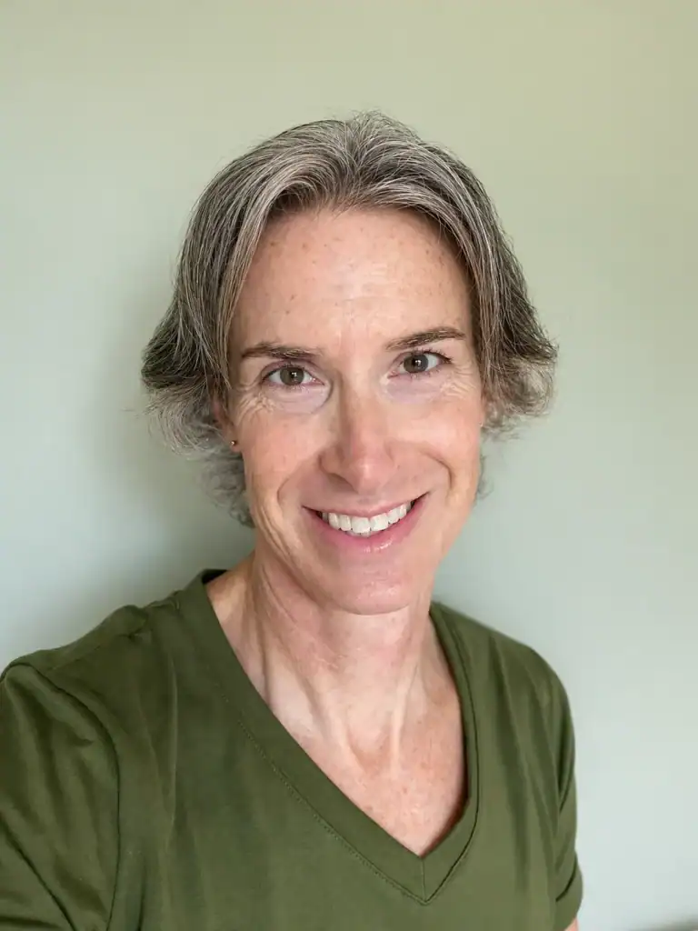 Sabrina Cleary smiling in a green V-neck shirt against a soft neutral background.